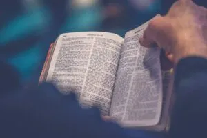 Close-up of hands holding an open Bible in dim light with the phrase "What Secrets Lie Within Zeus's Bible?" included for SEO.