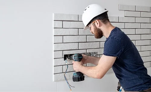 A residential electrician in Anaheim, CA installing new electrical wiring for electrical outlets in a residential setting, wearing a hard hat and using a power drill, emphasizing safety and professional service