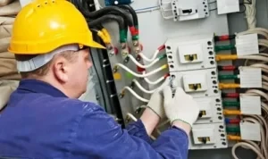 a commercial electrician in a yellow hard hat repairing an industrial electrical panel with colorful wiring, emphasizing commercial electrical services in Orange County.