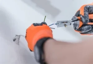 close up of an electrician's hands wearing safety gloves while installing electrical wiring and using electrical pliers to strip the new electrical wiring