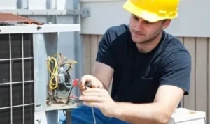 a technician wearing a yellow hard hat repairing the electrical wiring on an outdoor HVAC system