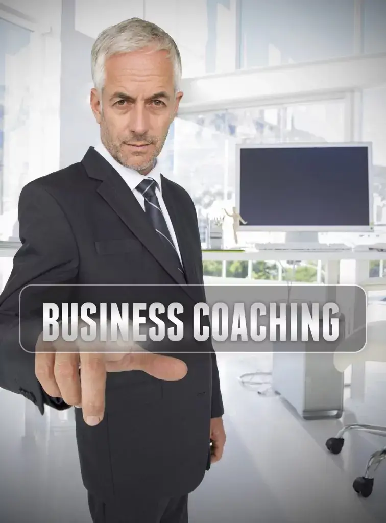 A man in a suit pointing at a translucent "Business Coaching" text overlay in a modern office setting.
