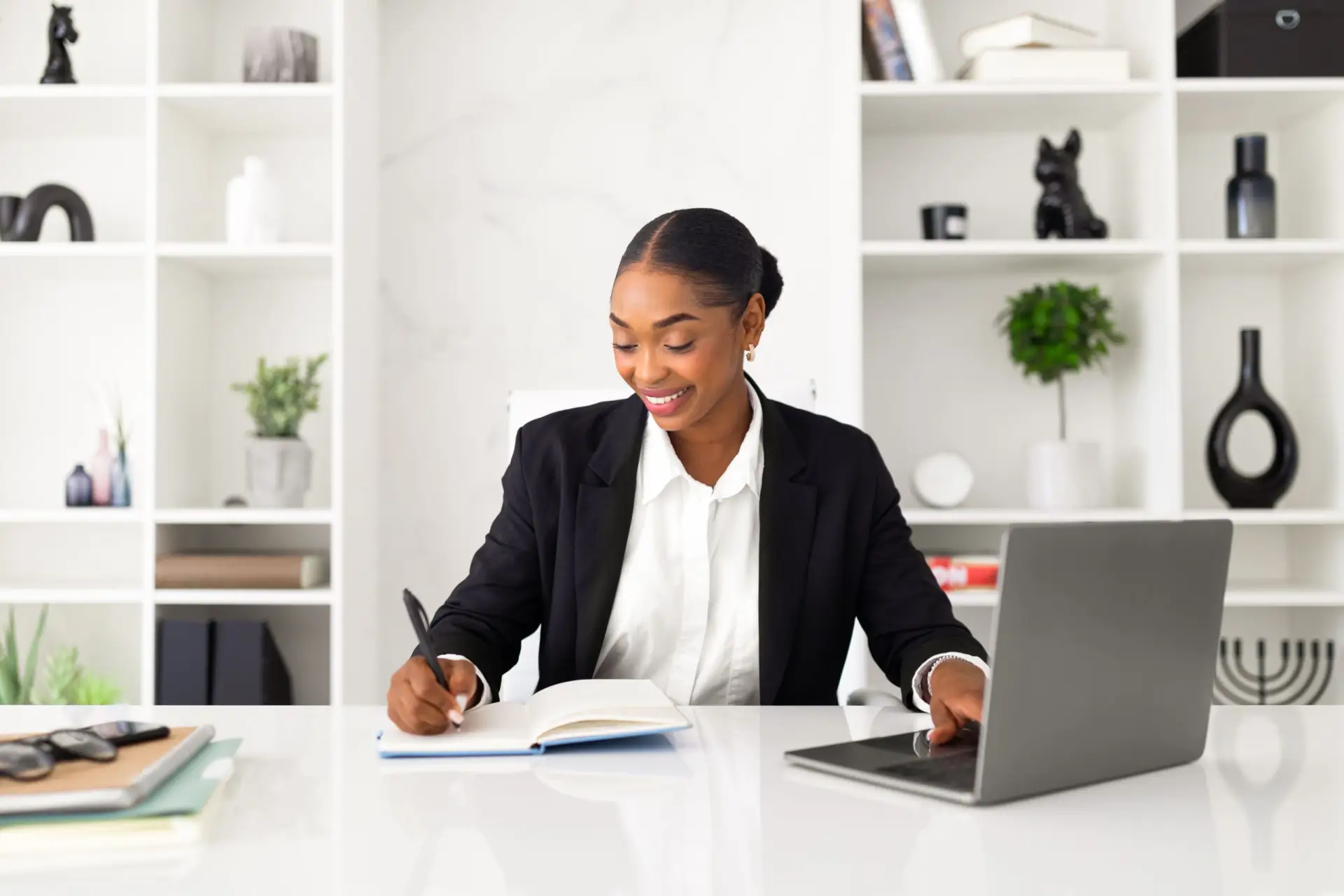 Professional Industrial Psychologist writing notes at a desk with laptop, bookshelf in background.
