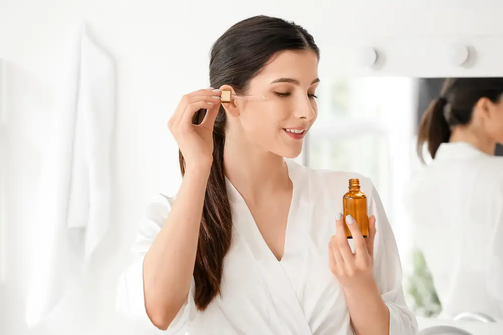 Beautiful young woman applying facial serum in bathroom to boost collagen in skin