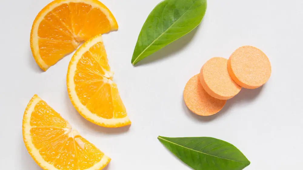 Top view of vitamin c effervescent tablets with fresh juicy orange fruit slice and green leaf on white table. Vitamins from foods or supplements choices. Health and medical concept.
