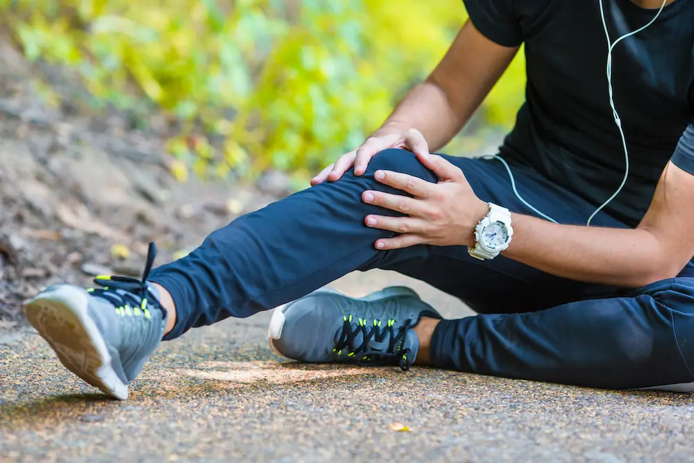 Male athlete suffering from pain in knee while exercising outdoor