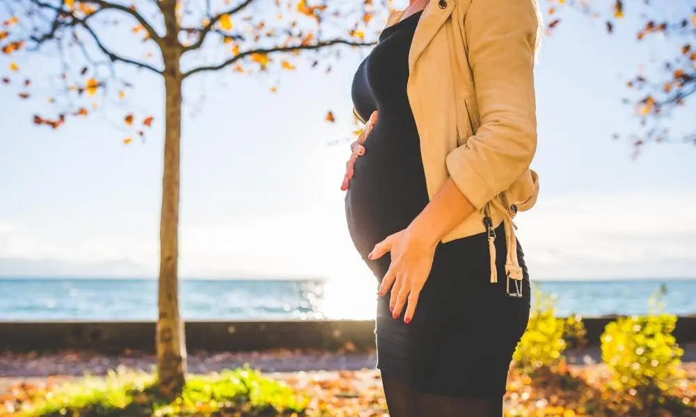 Pregnant woman holding stomach in park by water