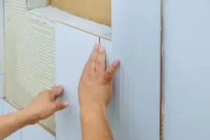 Fabre Occitanie - Une personne appliquant du mastic silicone Fabre sur l'espace entre un mur blanc et un climatiseur.