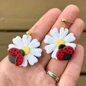 Handmade white daisy and red ladybug earrings with yellow centers.