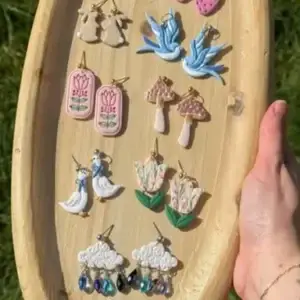 Colorful handmade clay earrings in diverse shapes: birds, bunnies, flowers, mushrooms, swans, clouds.