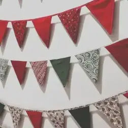 Three rows of red, green, and patterned fabric bunting hang on a white wall.