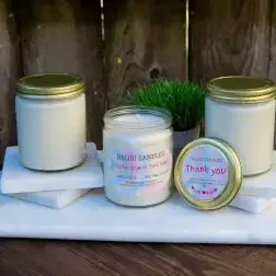 Three white jar candles with gold lids on marble. One open lid reads "Thank You.