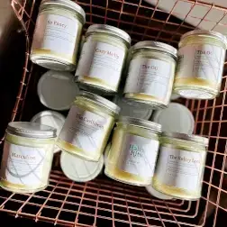 Eight pale yellow jar candles with white labels in a rose gold wire basket.