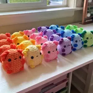 Rainbow-colored rows of adorable crocheted pig plushies on a white table.