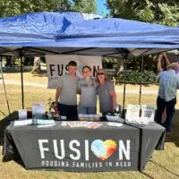 Smiling Fusion Housing team at their branded outdoor booth, ready to engage.