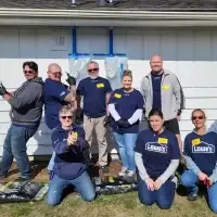 Nine cheerful Lowe's volunteers pose proudly in front of a house with mulch bags.