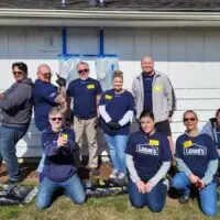 Smiling, diverse Lowe's volunteers pose outdoors with tools and mulch bags for a project.