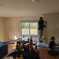 Three people painting a room: one on a chair, one on a ladder, one kneeling.
