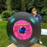 Smiling woman stands with a massive record prop, pink label reads 'Twistin' & Jumpin''.