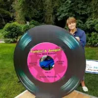 Smiling woman stands behind a giant vinyl record cutout with pink 'Twistin' & Jumpin'' label.