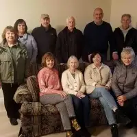 A group of ten smiling adults and seniors gathered informally, some standing, some seated on a couch.