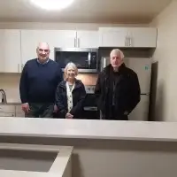 Three people, including two seniors, smile in a bright, modern kitchen.