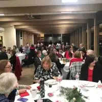 Large group of people dining and socializing at a festive indoor holiday party.