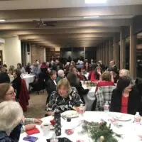 Many people enjoy a cheerful gathering, seated at tables with subtle holiday decorations.