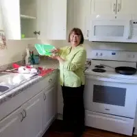 Smiling woman holds bright green plastic bowls in a clean, white kitchen.