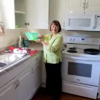 Smiling woman in a bright kitchen holding a green dish drying rack.