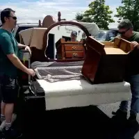 Two men loading a mirror, dresser, and other furniture into a truck bed.