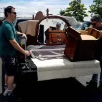 Two men load wooden furniture, including a mirrored dresser, into a pickup truck.