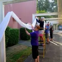 Several people decorating an outdoor covered walkway with flowing white fabric.