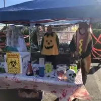 Three people in Halloween costumes: scientist, pumpkin, and hotdog, at a spooky, potion-filled table.
