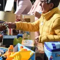 Woman in yellow puffer jacket exchanges object at a table laden with toys.