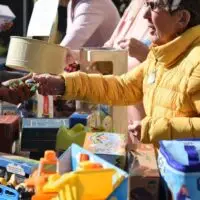 Woman in yellow jacket hands item to green-nailed person over a table of toys.