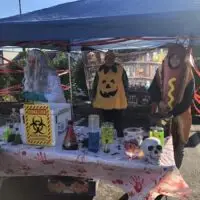 Outdoor Halloween event featuring costumed scientist, pumpkin, hot dog at a spooky science table.