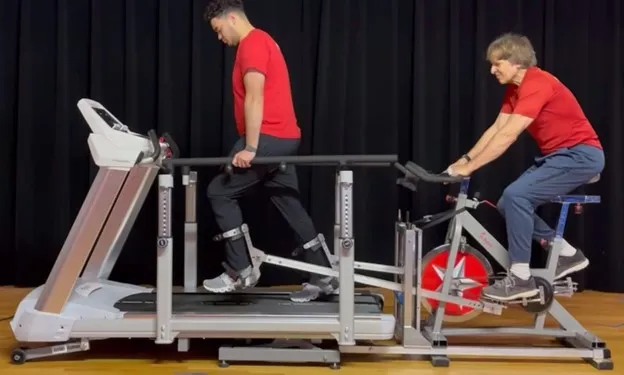 Person walking on TheraTrek gait trainer with other person on stationery bike assisting.