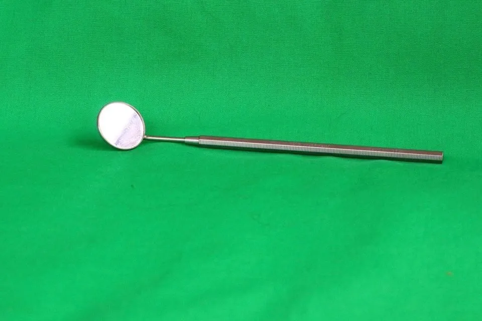 Dental mirror on a green background, the kind of tool a dentist uses to check a loose crown