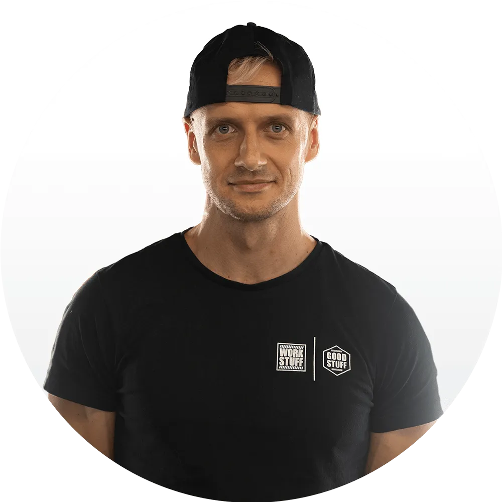A man wearing a black t-shirt with “Work Stuff” and “Good Stuff” logos and a backward black cap, standing against a plain white background.