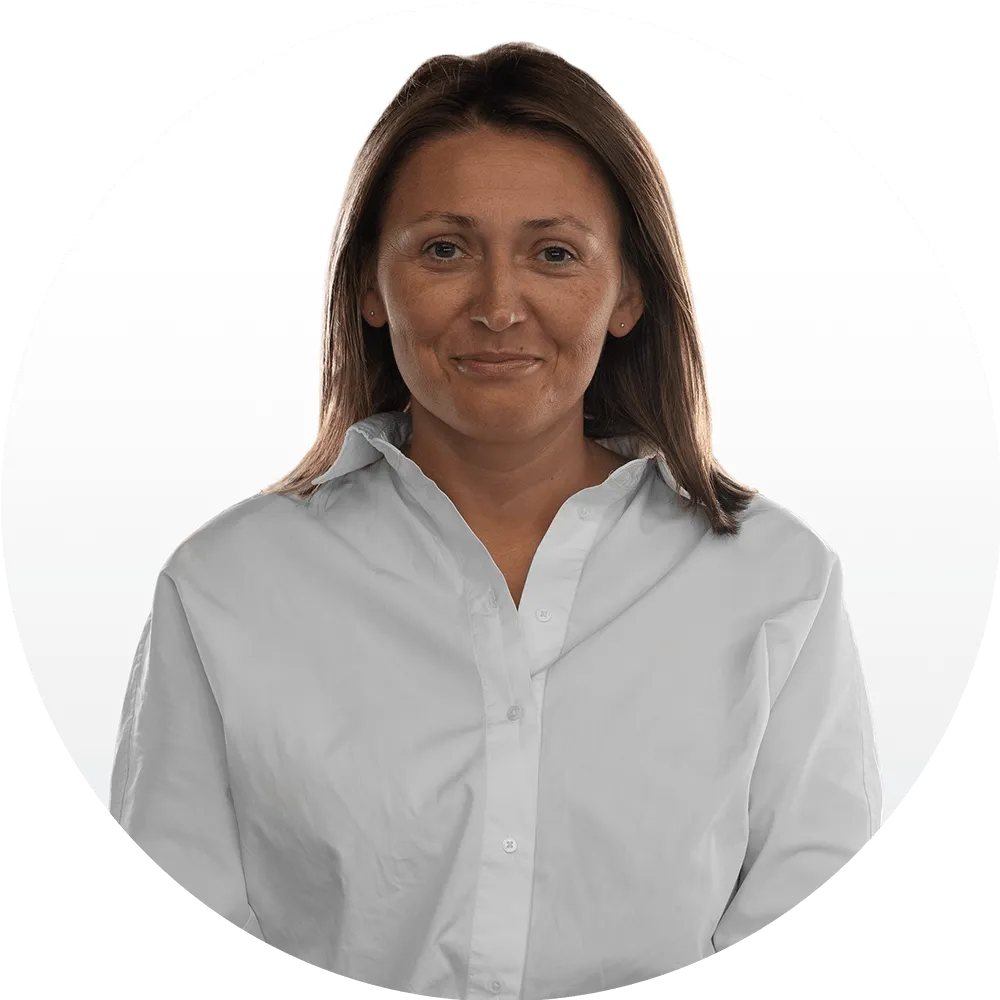 Woman with straight brown hair wearing a white button-up shirt, standing against a plain white background, looking directly at the camera with a slight smile.