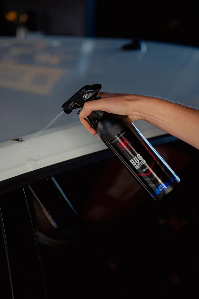 A person uses Bug Buster, a powerful bug remover, to spray and clean a stubborn bug mark from the roof of a white car, exemplifying effective car bug cleaning. A person uses Bug Buster, a powerful bug remover, to spray and clean a stubborn bug mark from the roof of a white car, exemplifying effective car bug cleaning.