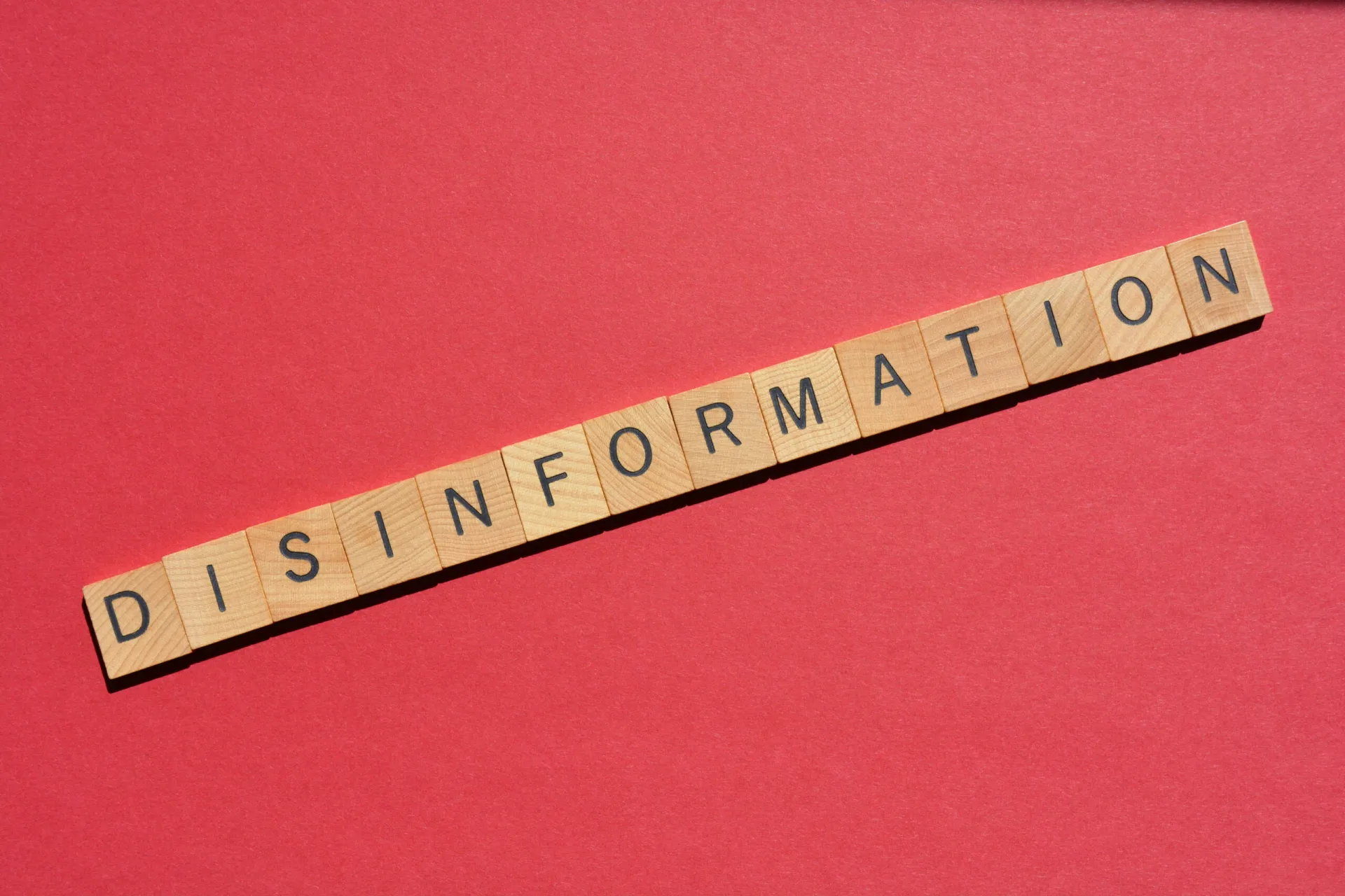 Hölzerne Buchstabenkacheln mit der Aufschrift DISINFORMATION" sind in einer geraden Linie auf rotem Hintergrund angeordnet und spiegeln Online-Trends wie ADHS Diagnose TikTok" und die Verbreitung von Fehlinformationen über psychische Gesundheit wider.