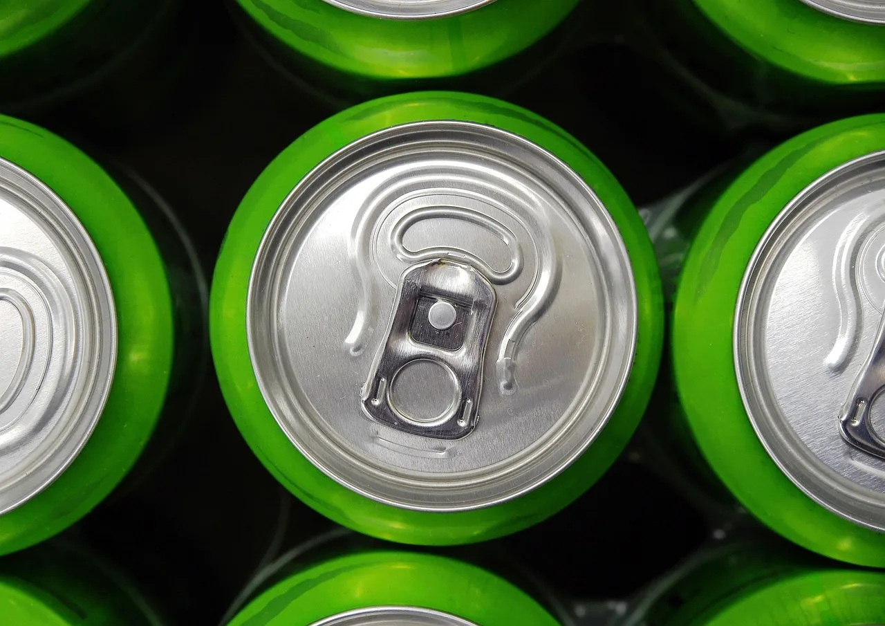 Nahaufnahme der Deckel mehrerer ungeöffneter grüner Softdrink-Dosen, die dicht nebeneinander angeordnet sind.
