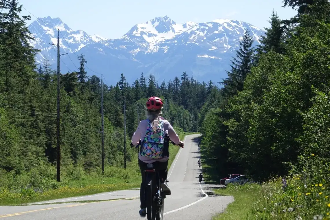 How to Explore Juneau Like a Local: Bike Rental Tips and Top Routes? 1 Juneau eBike tour ascending a road through Tongass National Forest with snow-capped mountains.