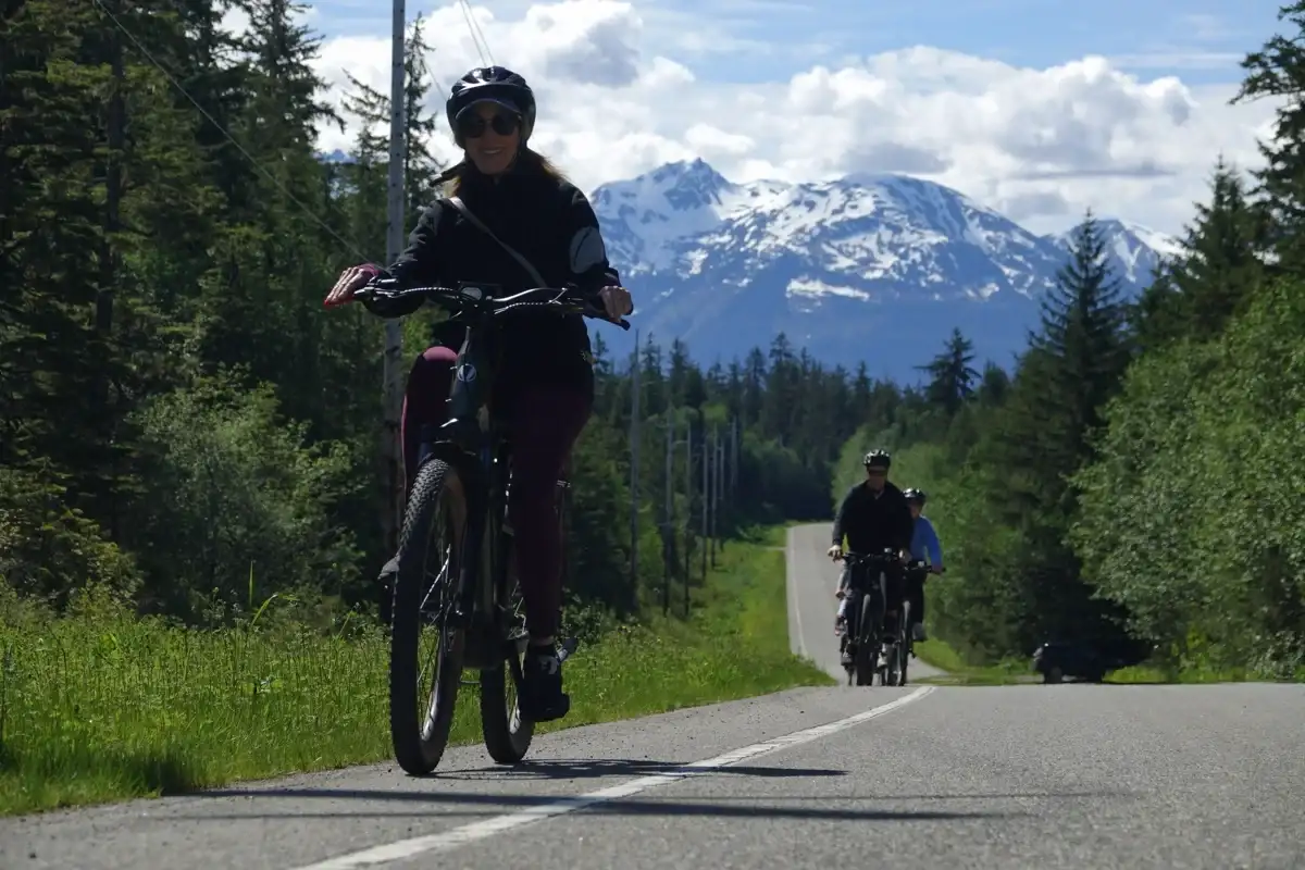 Eco-Friendly Tours in Juneau Alaska: Travel Green with iRide 2 Woman and group on an eBike tour through Juneau forest with snowy mountains.