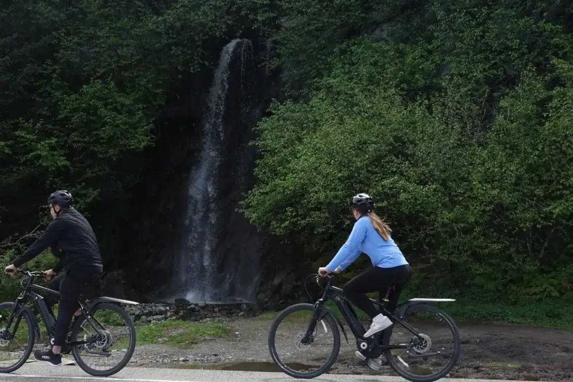 Hidden Gems in Juneau: The Best Places to Visit for Every Kind of Traveler 6 Two eBike riders pass a Juneau waterfall with dense green forest.
