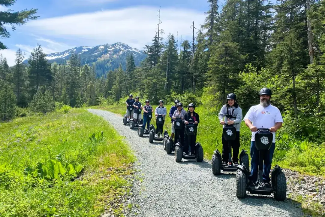 Juneau-alpine-segway-small-group-mountain-tour-smile-1200x800 Group on an iRide Alaska Juneau Segway tour on a forest trail with mountains.
