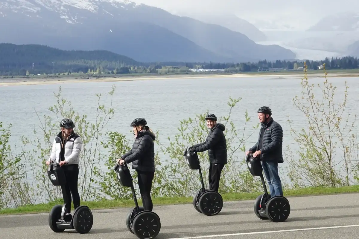 Four people on a Juneau Segway tour along a bay, with mountains and a glacier.