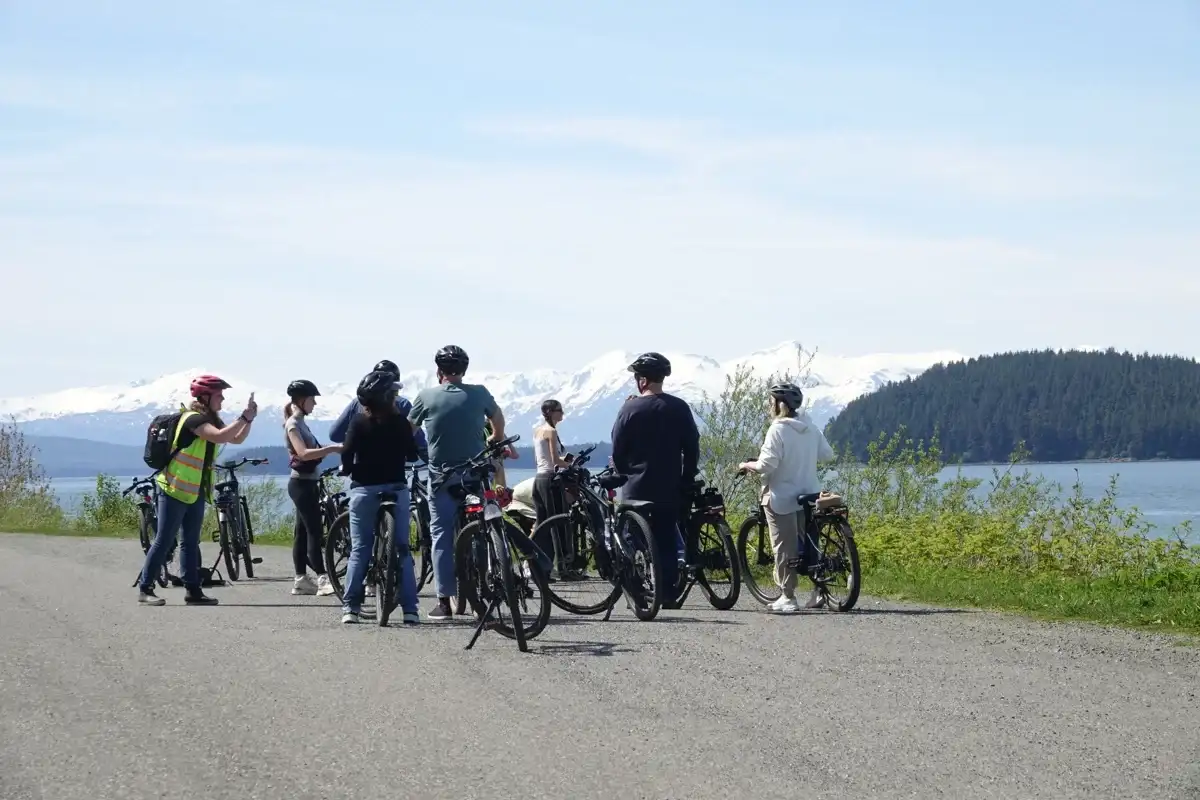 A Juneau eBike tour group pauses to photograph snow-capped mountains and coastal forest.